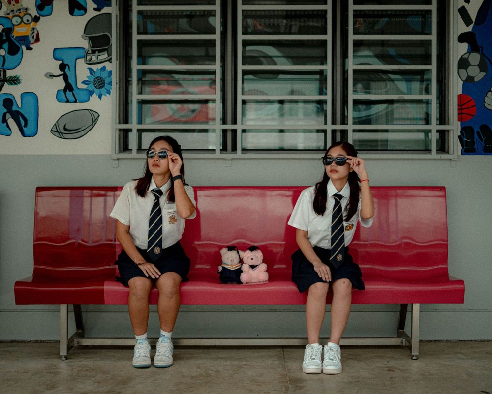 Students in matching uniforms pose on red bench with sunglasses.
