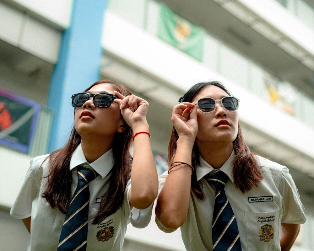 Students in school uniforms adjusting sunglasses outdoors on campus.