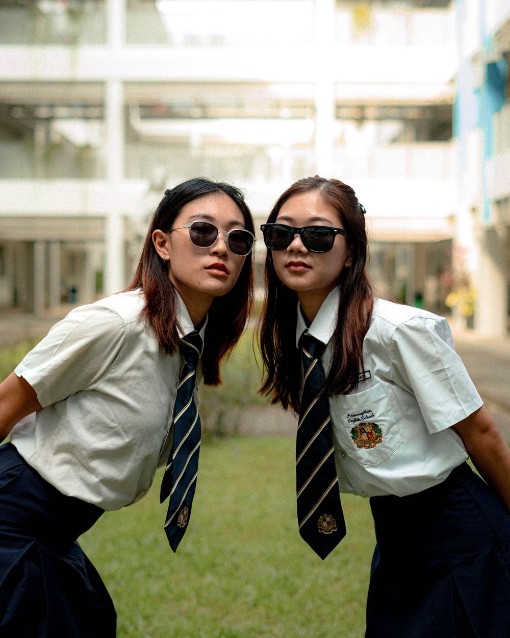 Students in school uniforms and sunglasses pose together on campus grounds.
