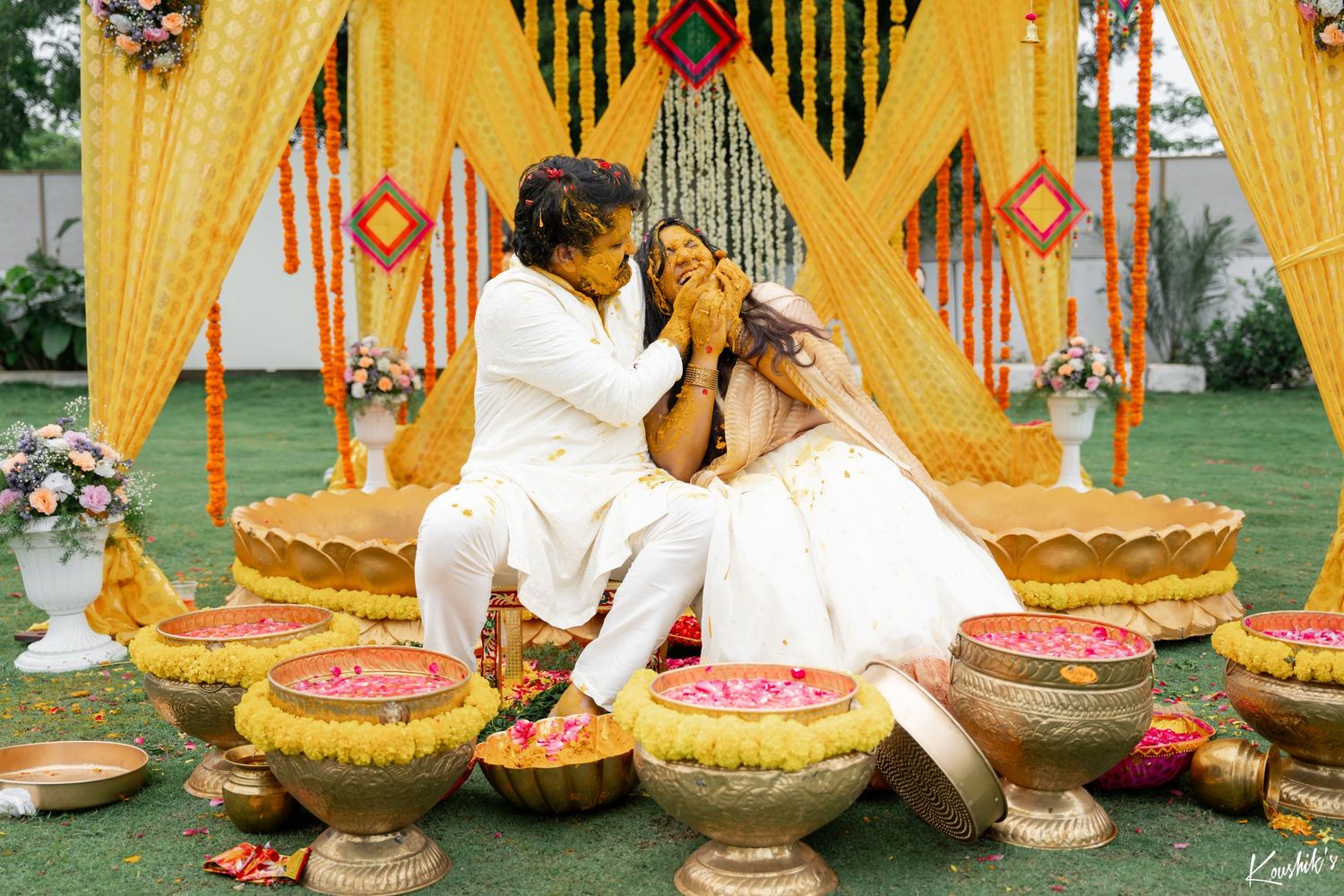 Traditional Indian wedding ceremony setup with yellow decor and floral arrangements in brass vessels on grass.