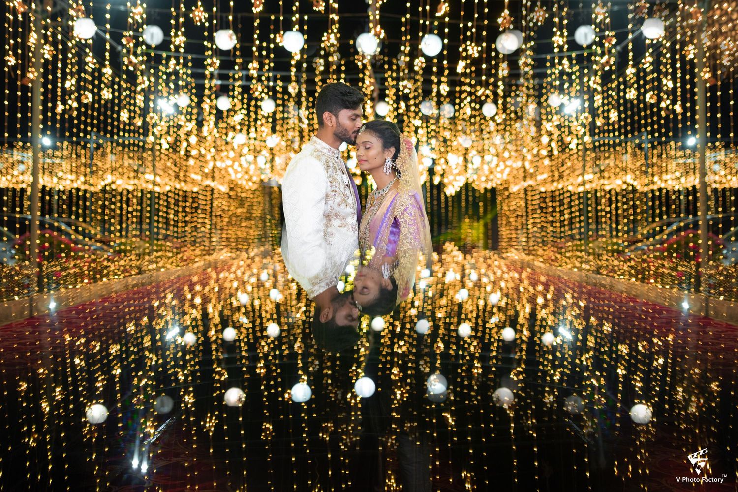 A romantic couple stands under a stunning canopy of twinkling lights creating an ethereal tunnel reflection effect.