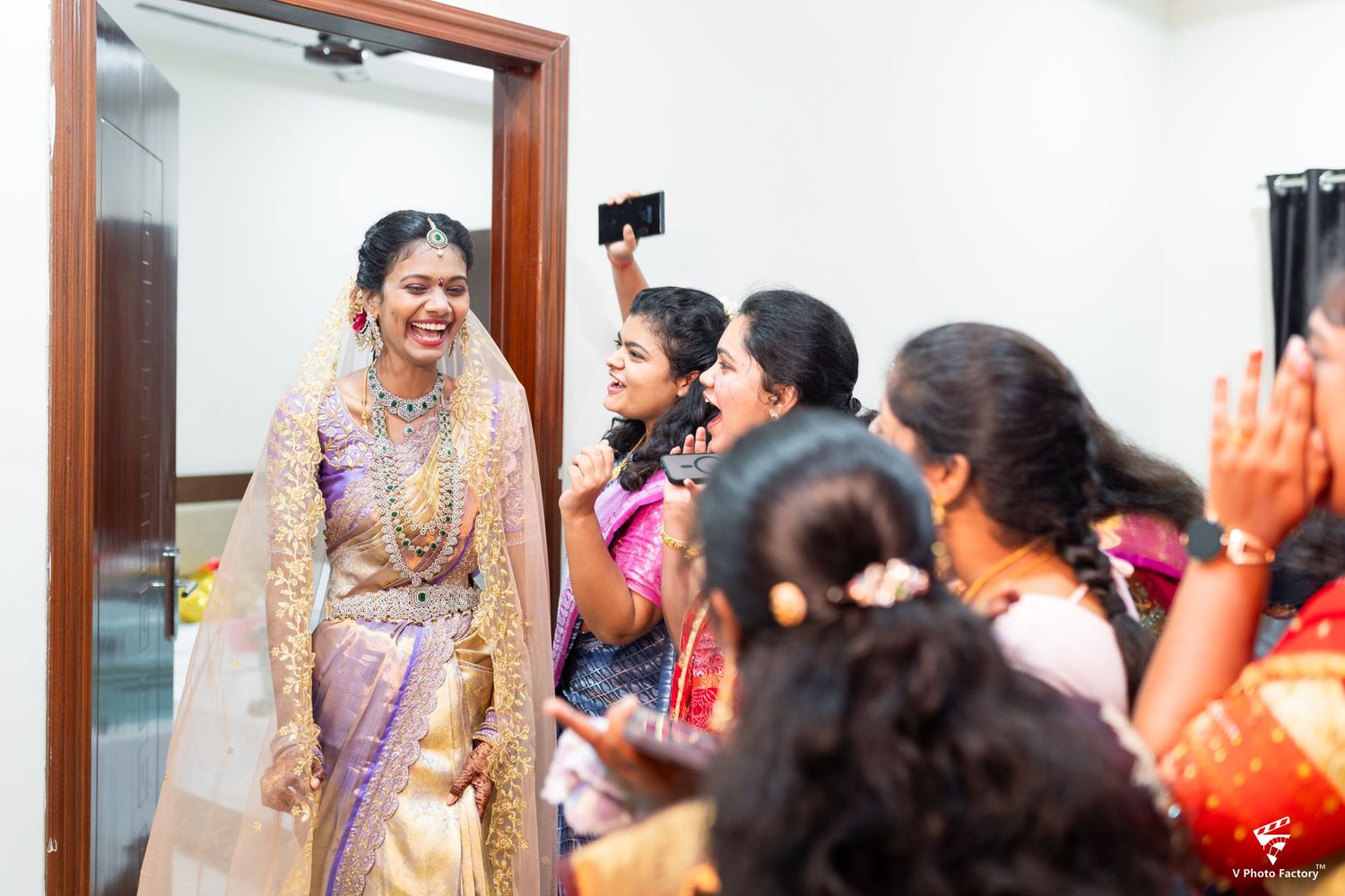A traditional Indian wedding celebration with guests in colorful saris and formal attire gathered in a bright indoor setting.