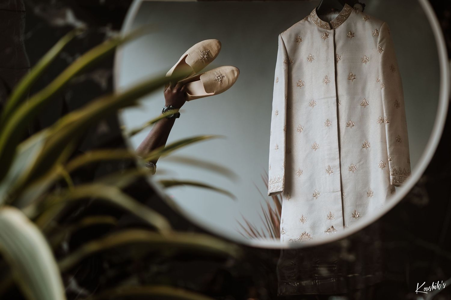 A white linen dress shirt hangs near a round mirror with ballet pointe shoes and green plants in view.
