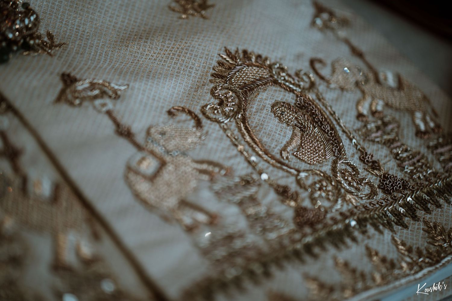 Close-up shot of ornate embroidered design with a monogram crest pattern on textured fabric in sepia tones.