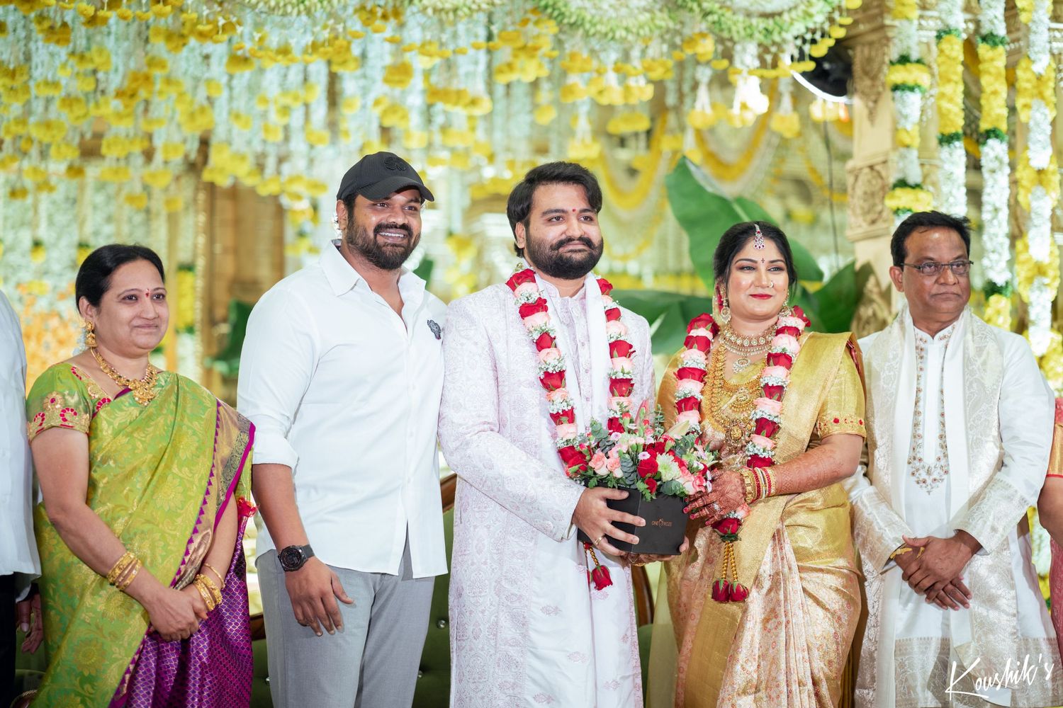 Traditional South Indian wedding ceremony with participants wearing traditional attire under yellow floral decorations.