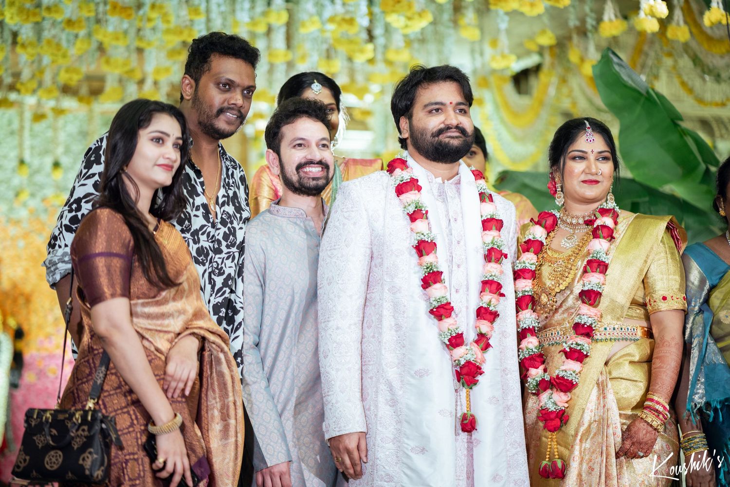 A group celebrates at a festive event with decorative garlands and yellow floral decor in the background.