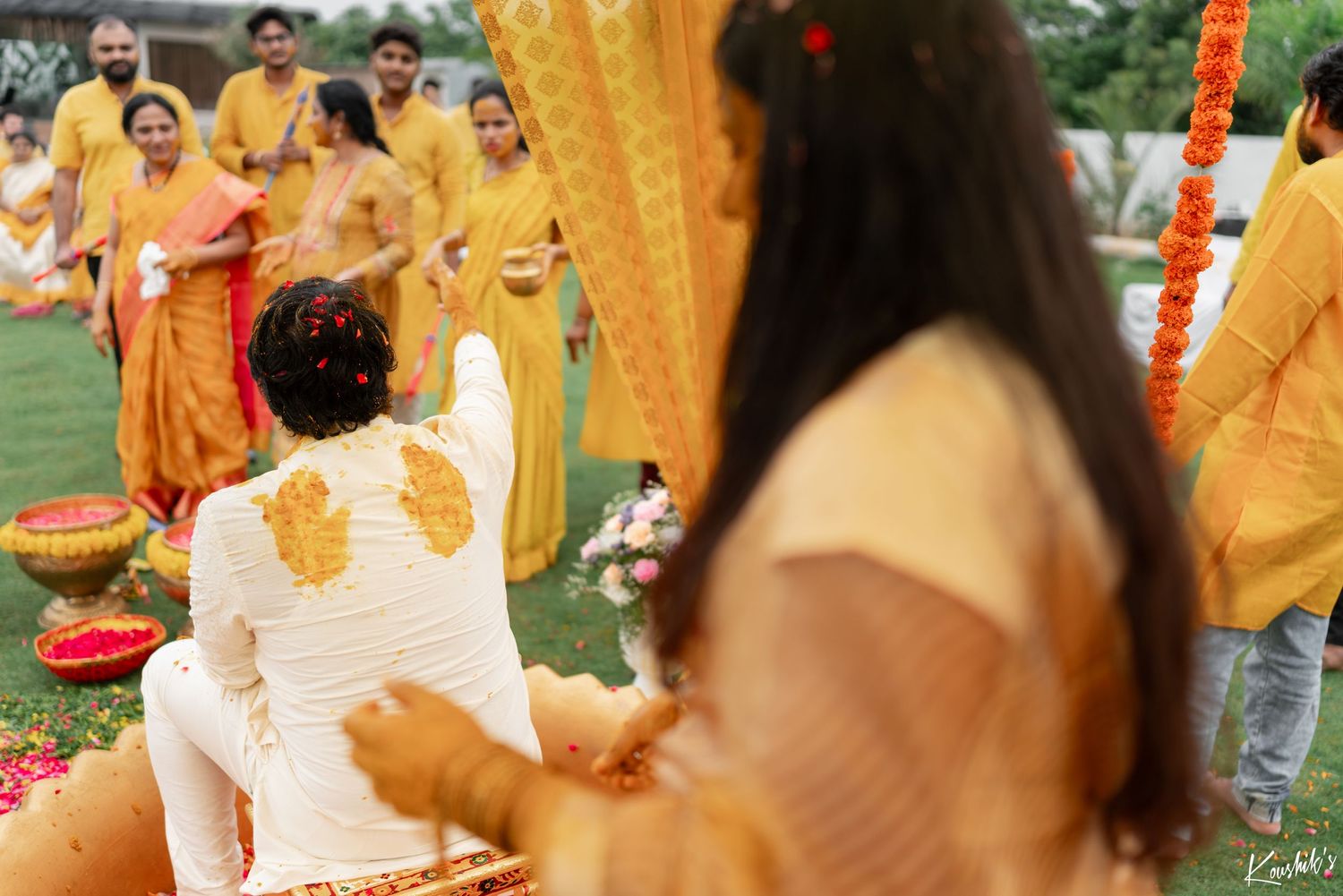 A blurred motion shot of a traditional Indian wedding ceremony with people wearing yellow and white attire in an outdoor setting.