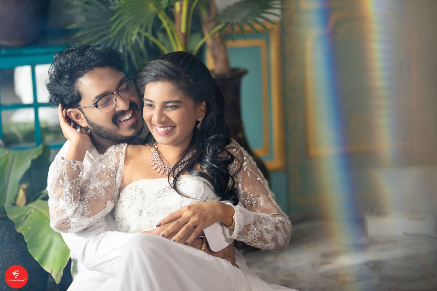 A couple sharing a joyful moment in elegant white outfits amid a tropical decor setting.