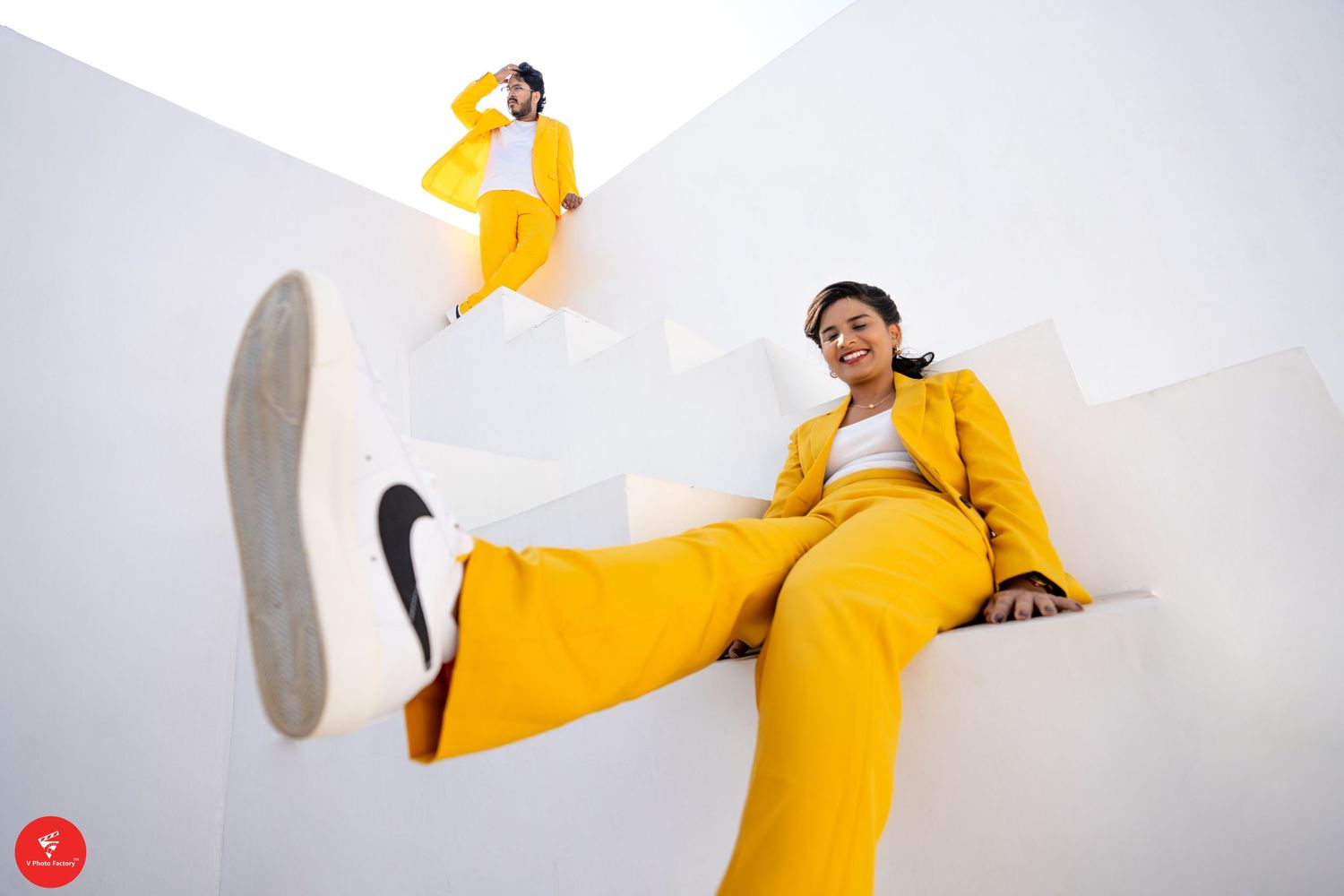 Person in vibrant yellow outfit lounging sideways on white surface with kicking motion and black Nike sneakers.