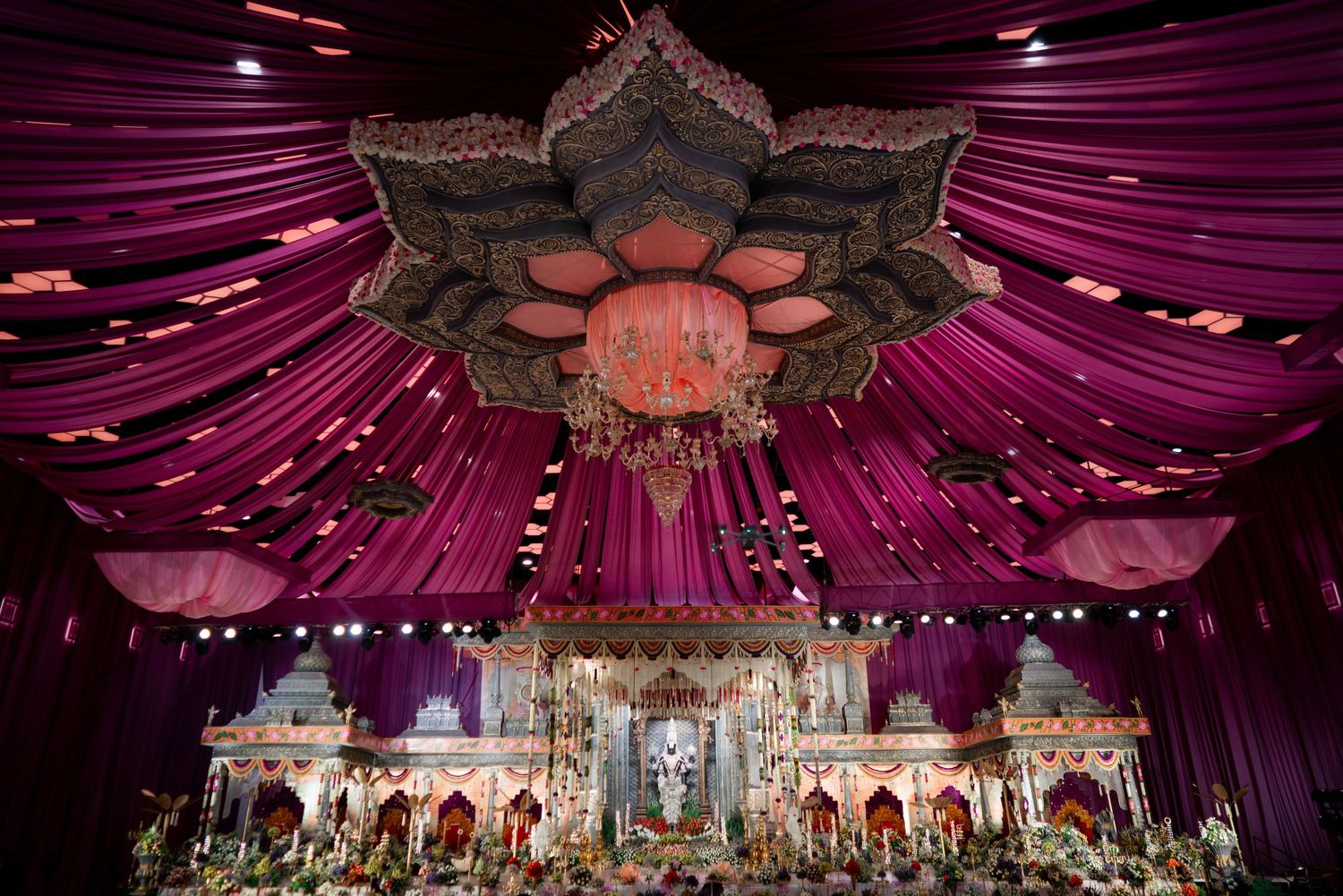Ornate wedding reception venue with dramatic purple draping, floral chandelier and luxurious stage backdrop.