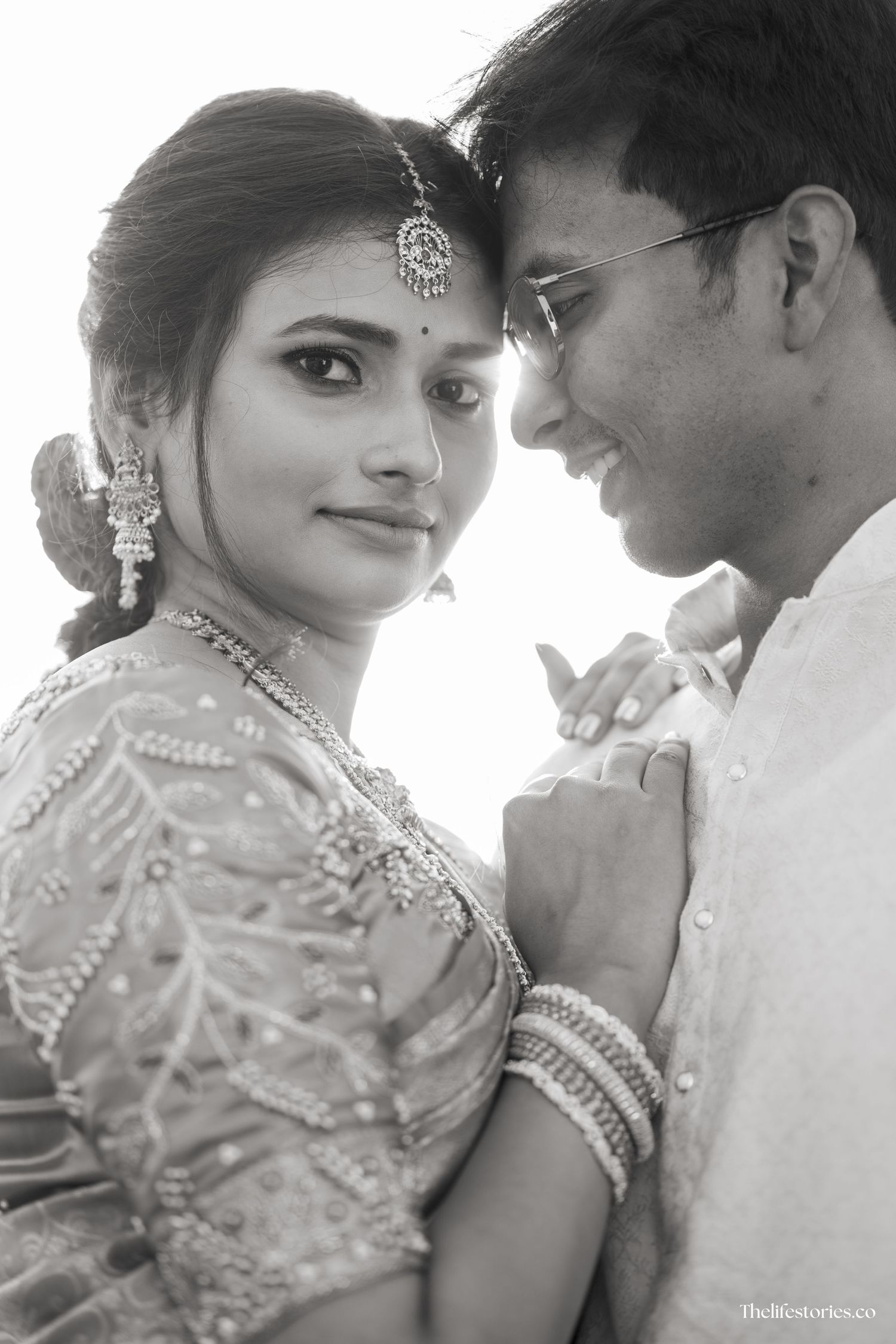 A black and white portrait of a couple in traditional Indian wedding attire with the bride wearing ornate jewelry and saree.
