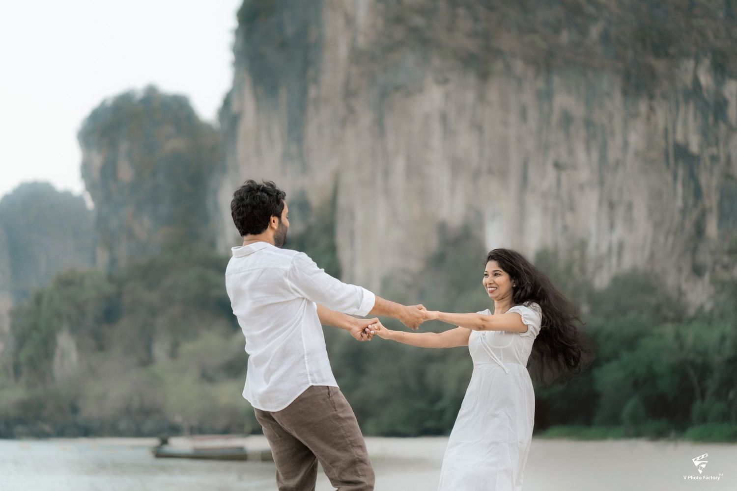 A couple dancing together near a scenic limestone cliff by the water at sunset.