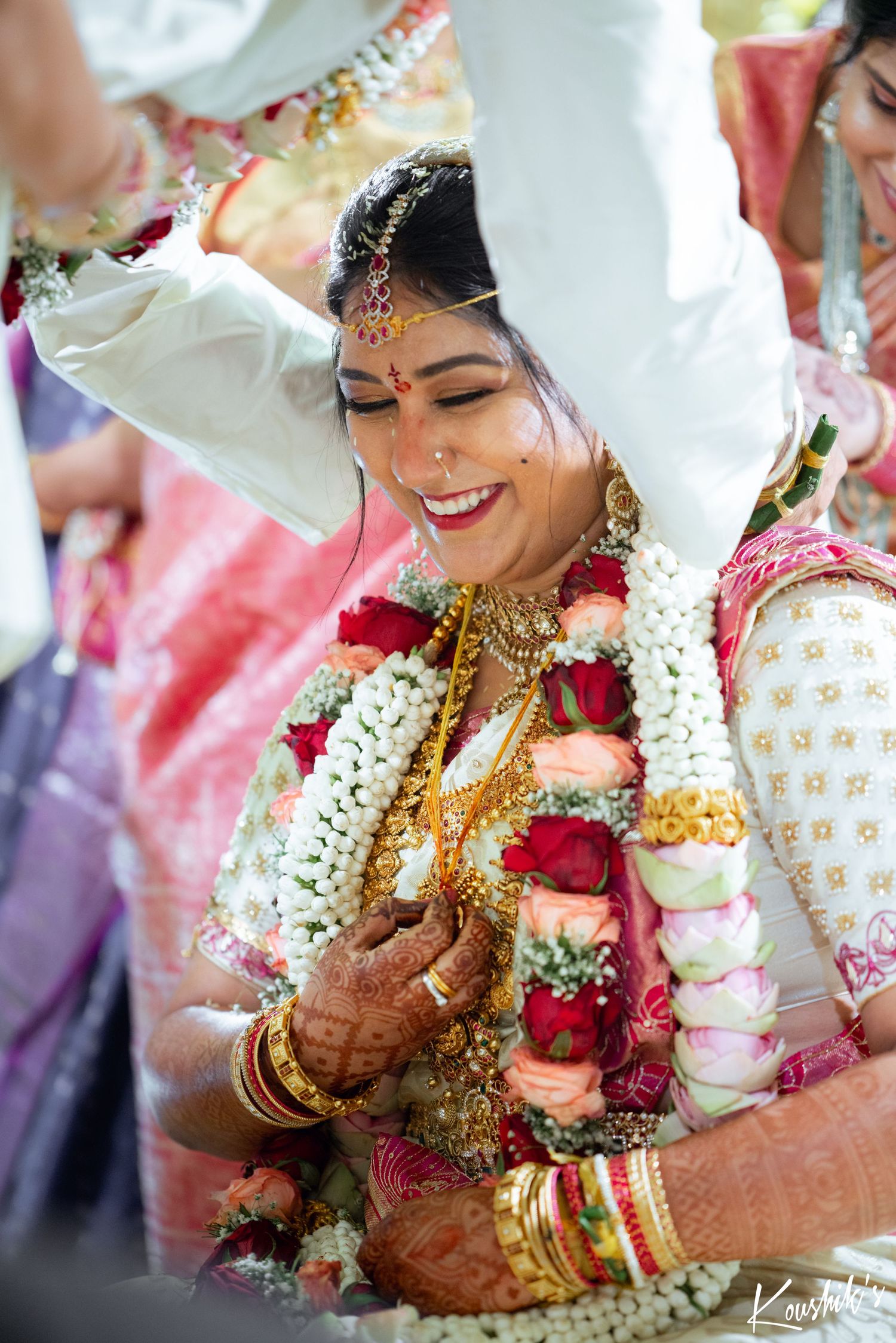 South Indian bride wearing traditional gold jewelry and floral garlands smiles during a wedding ceremony ritual.