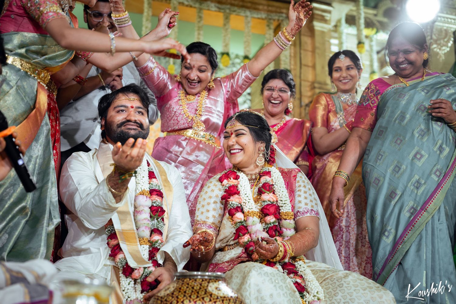 A joyous traditional Indian wedding ceremony with guests celebrating as the couple shares a candid moment wearing floral garlands.