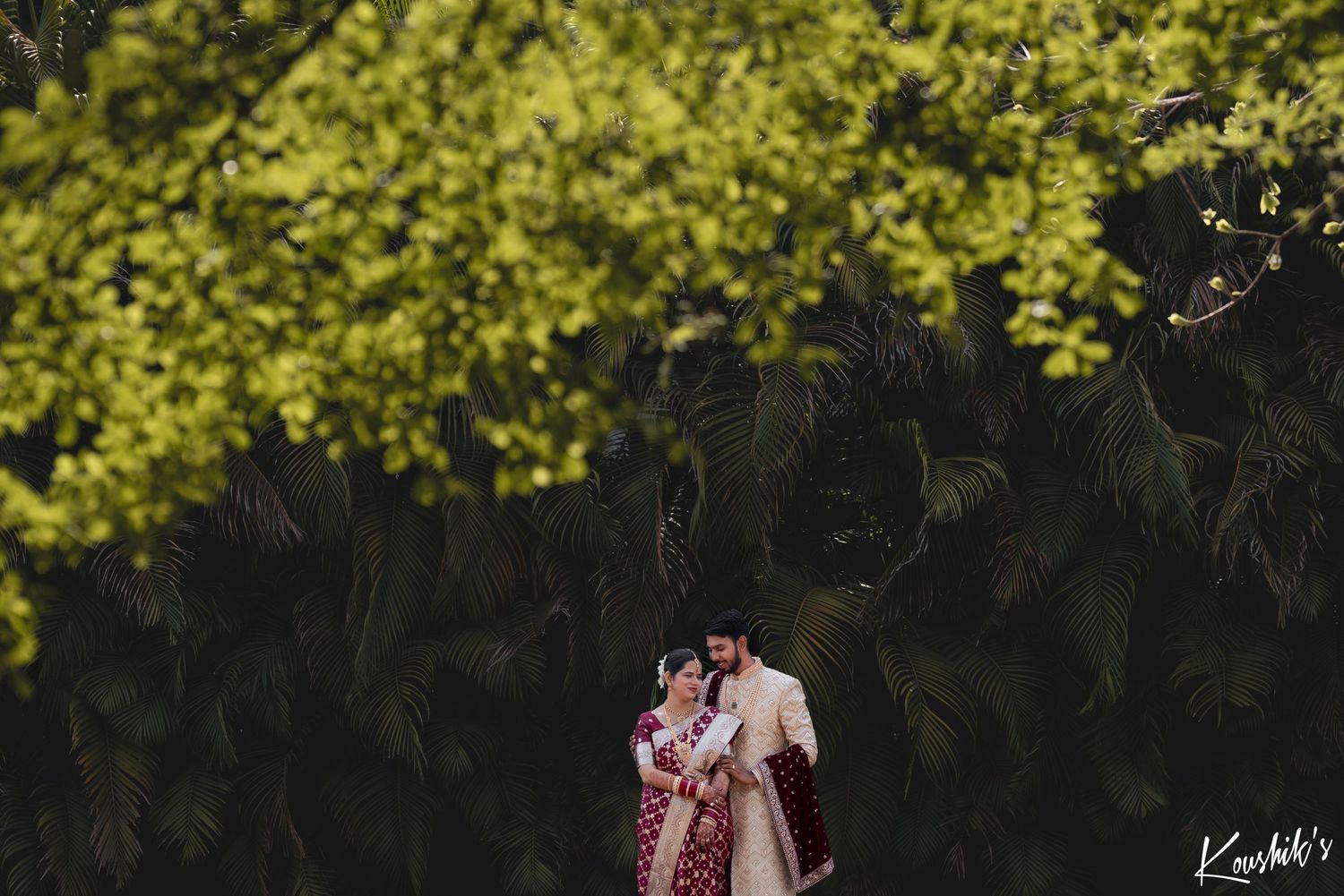 Couple embraces under glowing yellow autumn trees in artistic wedding photography shot.