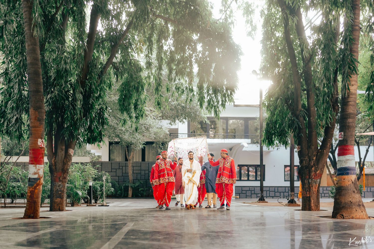 Traditional Chinese wedding party walking down a tree-lined path with red decorations and lanterns.