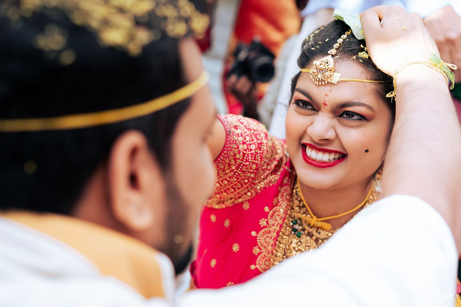 A joyful moment captured during a traditional Indian wedding ceremony with vibrant red and gold attire.