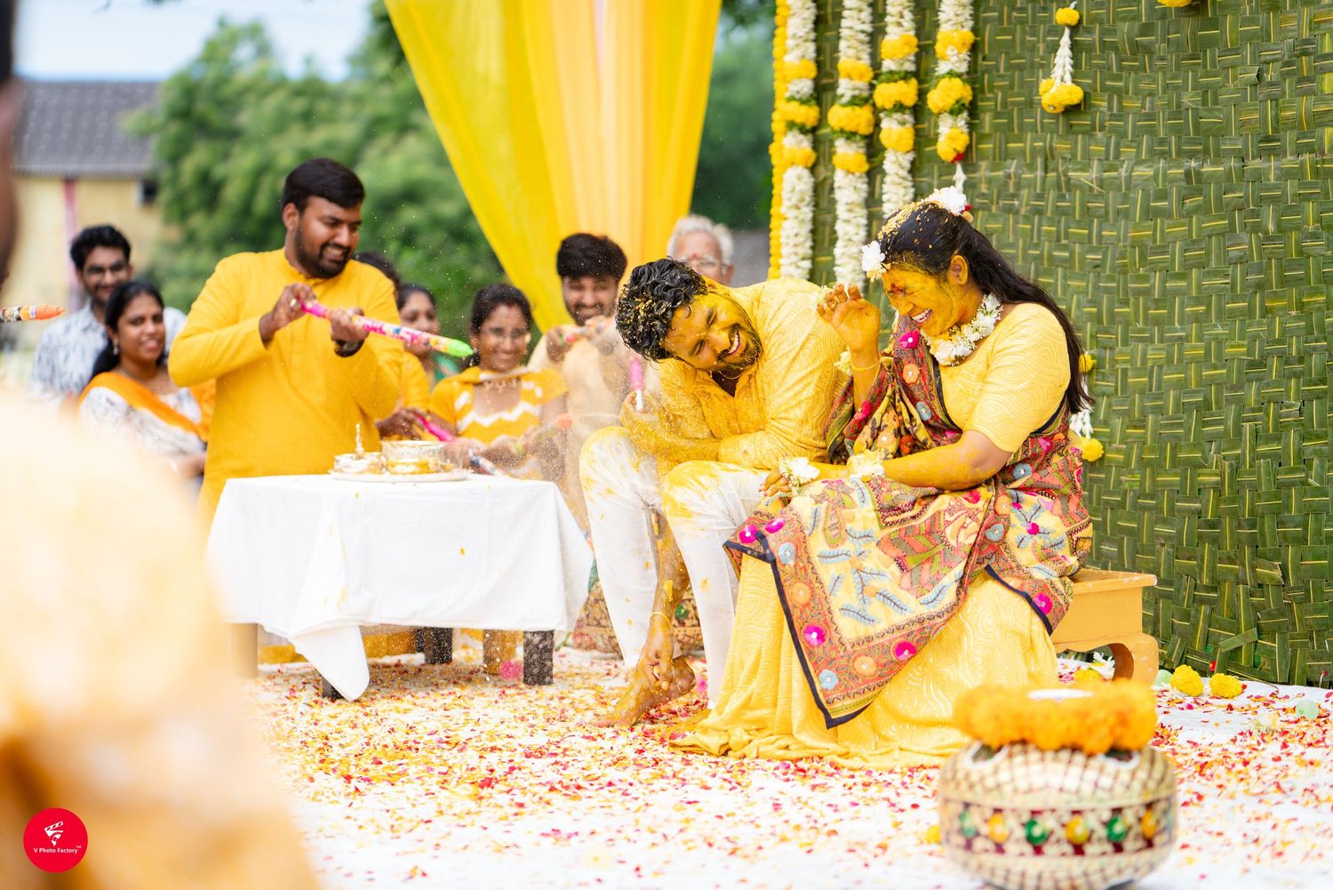 Celebration at traditional Indian wedding with yellow decor and flower petals scattered on the floor during haldi ceremony.