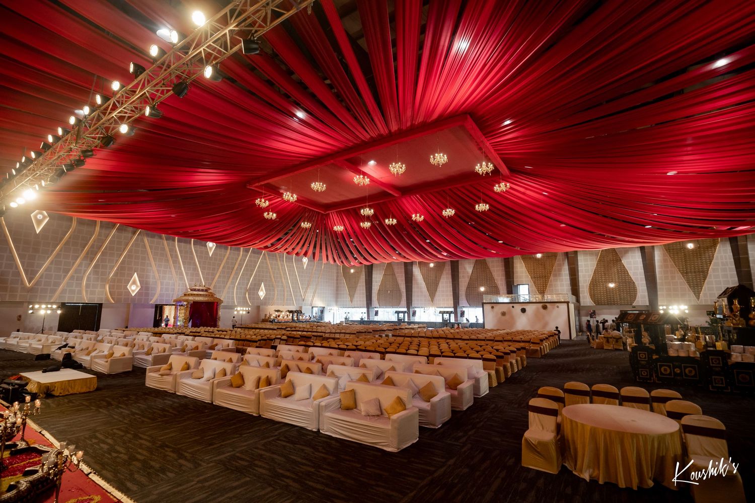 Elegant wedding reception venue with dramatic red draped ceiling, round tables, and ambient lighting creating a luxurious atmosphere.