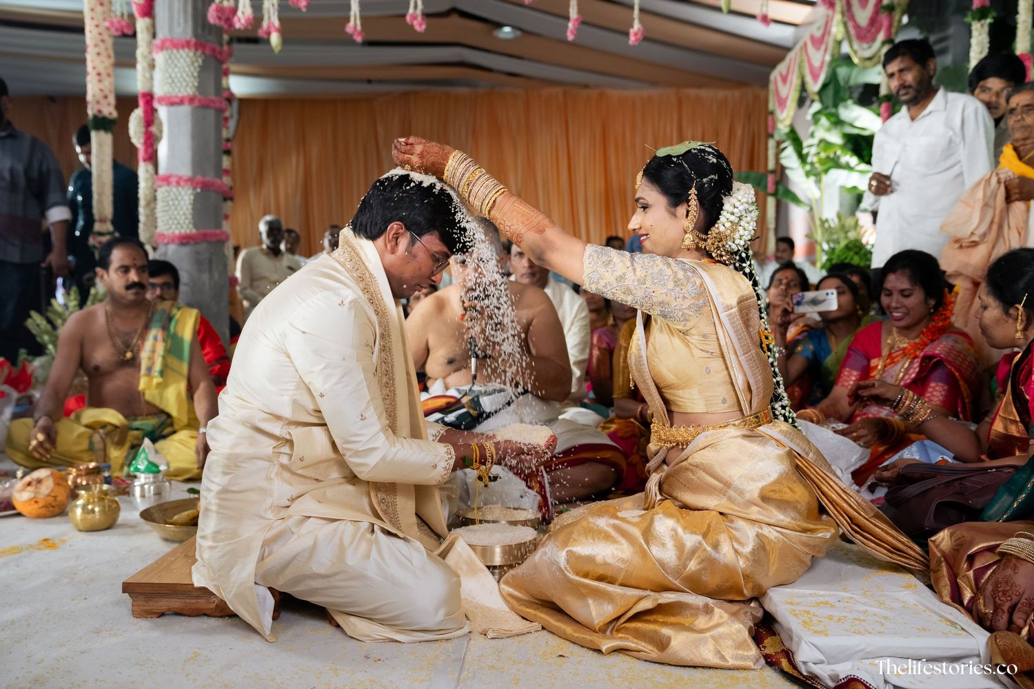 Traditional Indian wedding ceremony with couple performing ritual in traditional gold and cream attire surrounded by decorations.