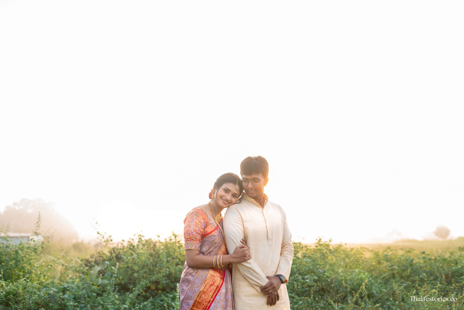 A romantic couple embraces in a sunlit field at sunset with golden light streaming through the background.