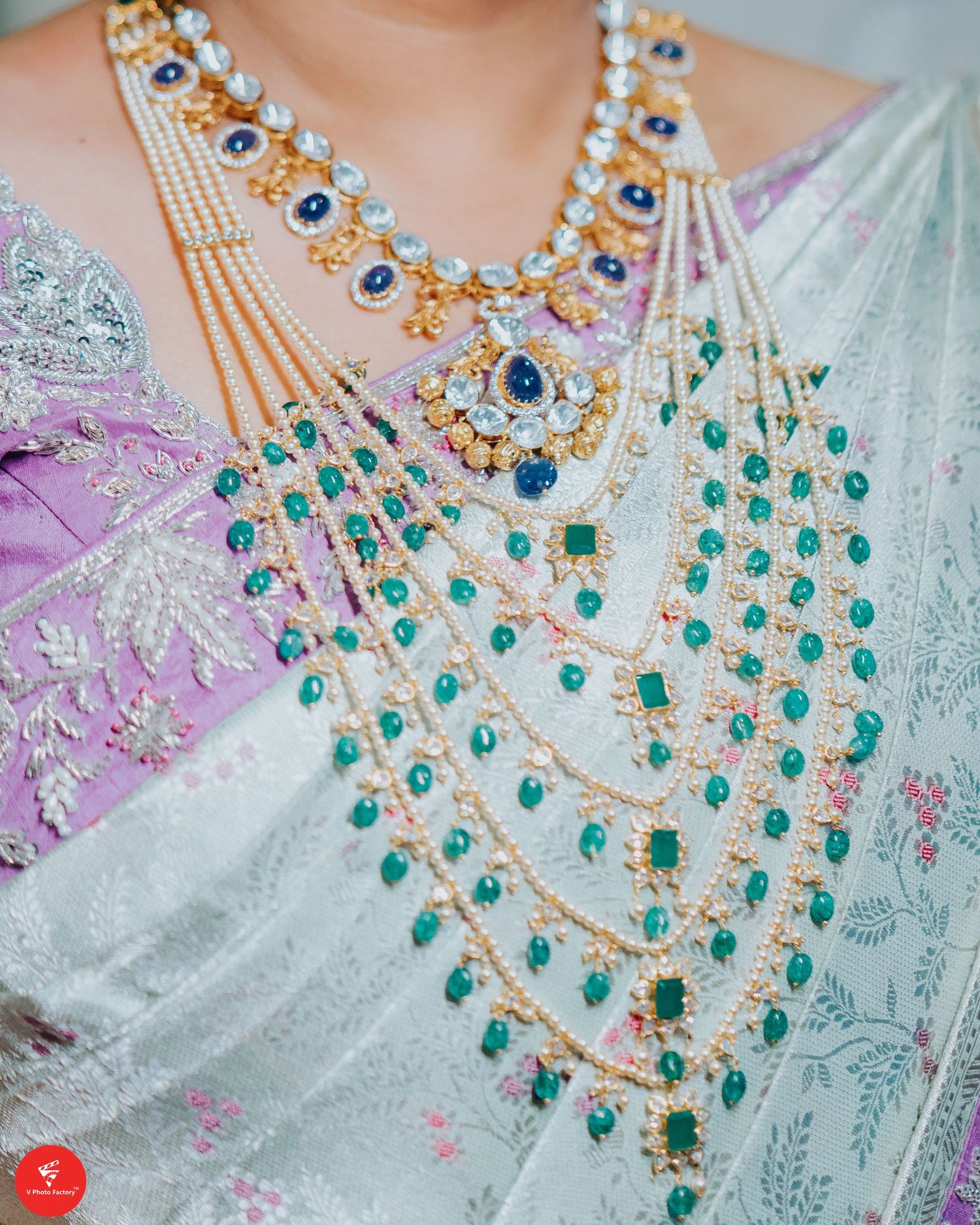 Layered traditional Indian bridal jewelry featuring blue sapphires and emerald stones on an ornate white and pink saree.