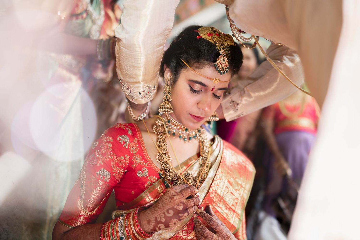 A bride in traditional Indian wedding attire with gold jewelry and a red sari prepares during her wedding ceremony.