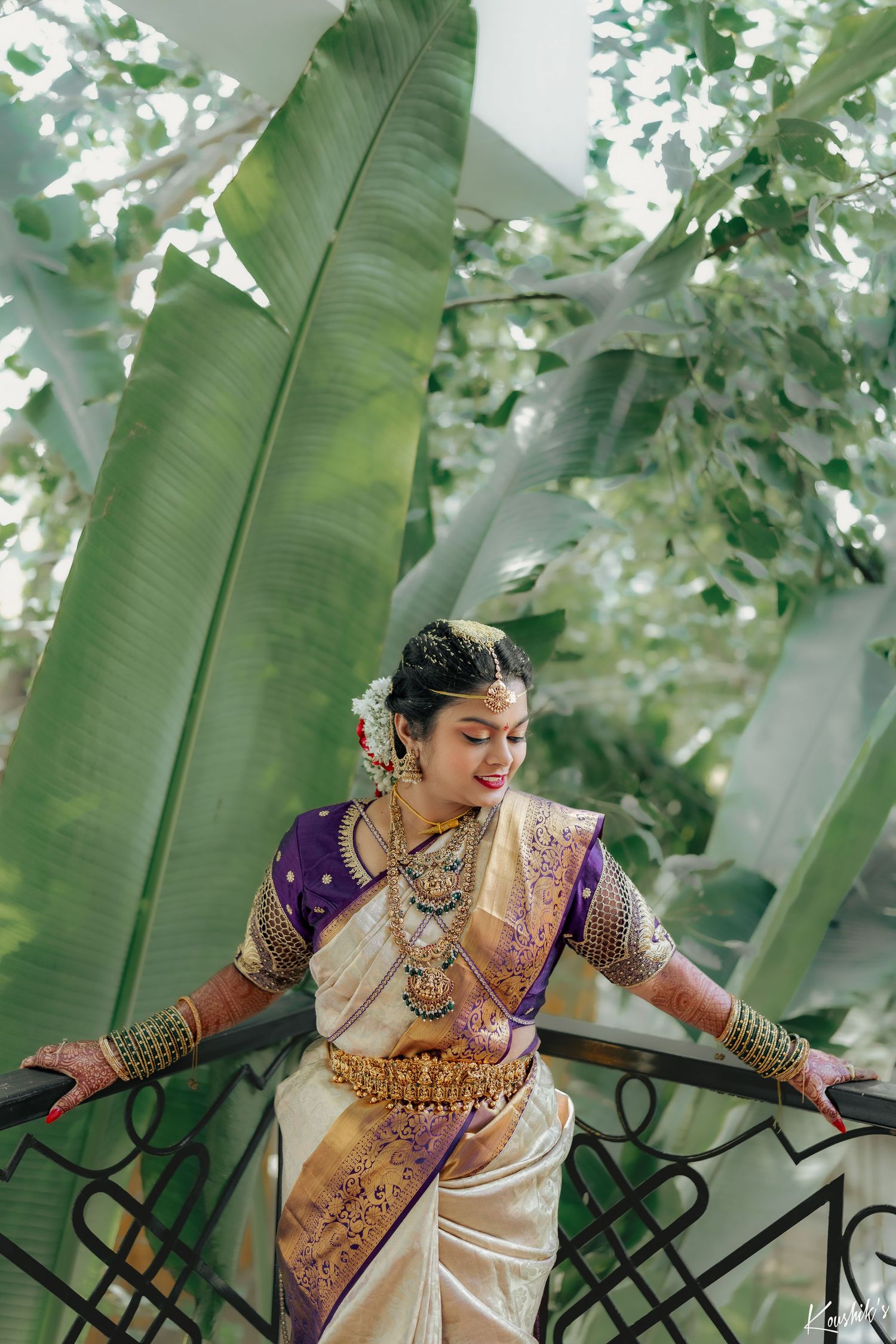 Traditional South Indian dance performer wearing ornate silk saree and gold jewelry poses gracefully among banana leaves.