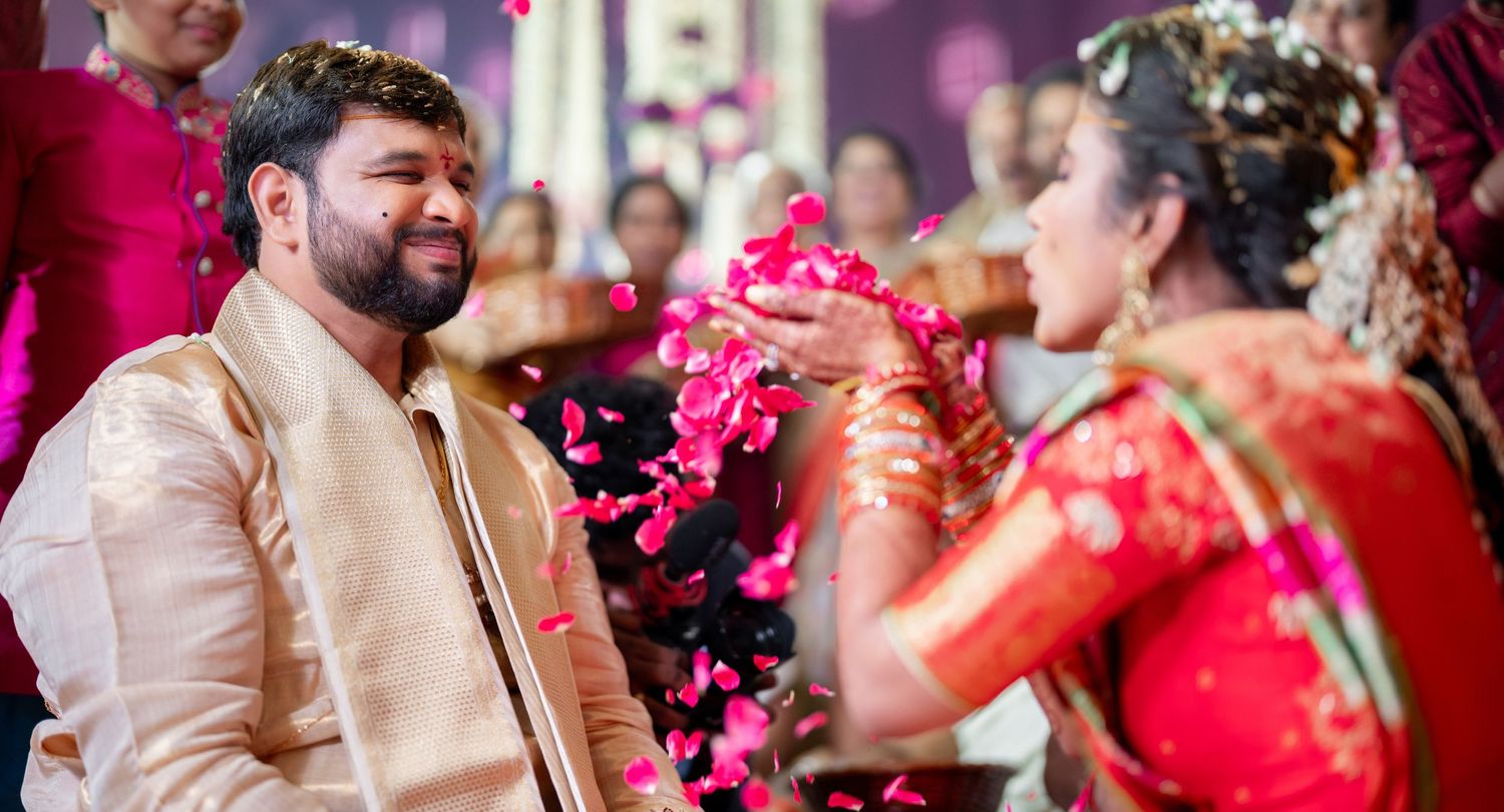 Traditional Indian wedding celebration with guests showering pink flower petals during a joyful ceremony moment.