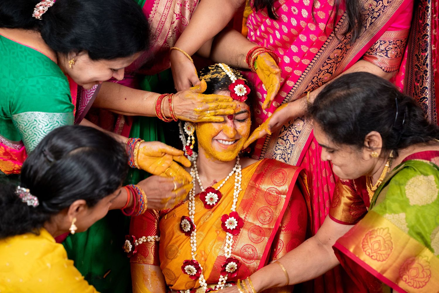 Traditional Indian Haldi ceremony during wedding celebration with turmeric paste being applied by women wearing colorful saris.