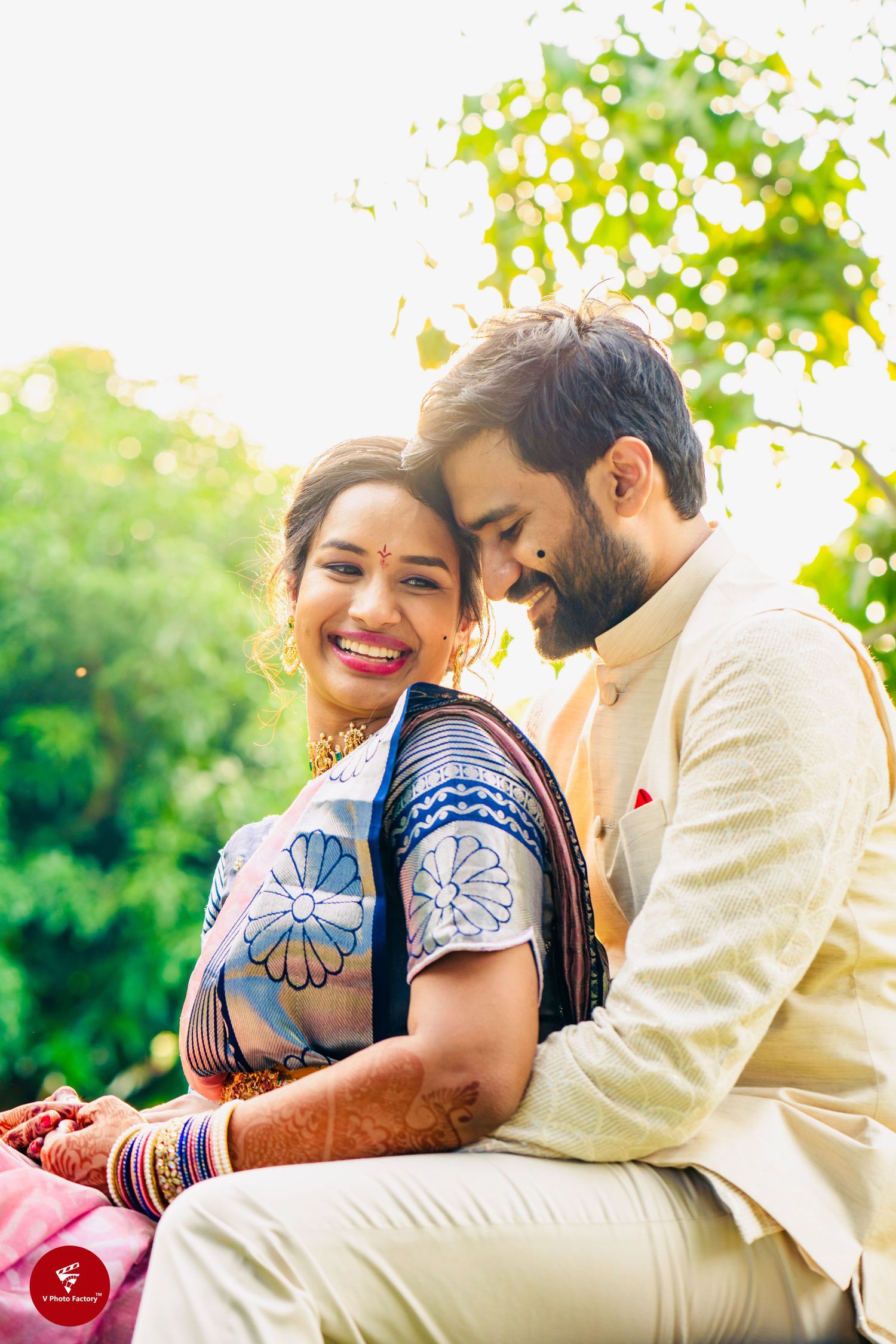 A couple shares an intimate moment outdoors, with the woman wearing a blue patterned outfit and the man in cream attire.