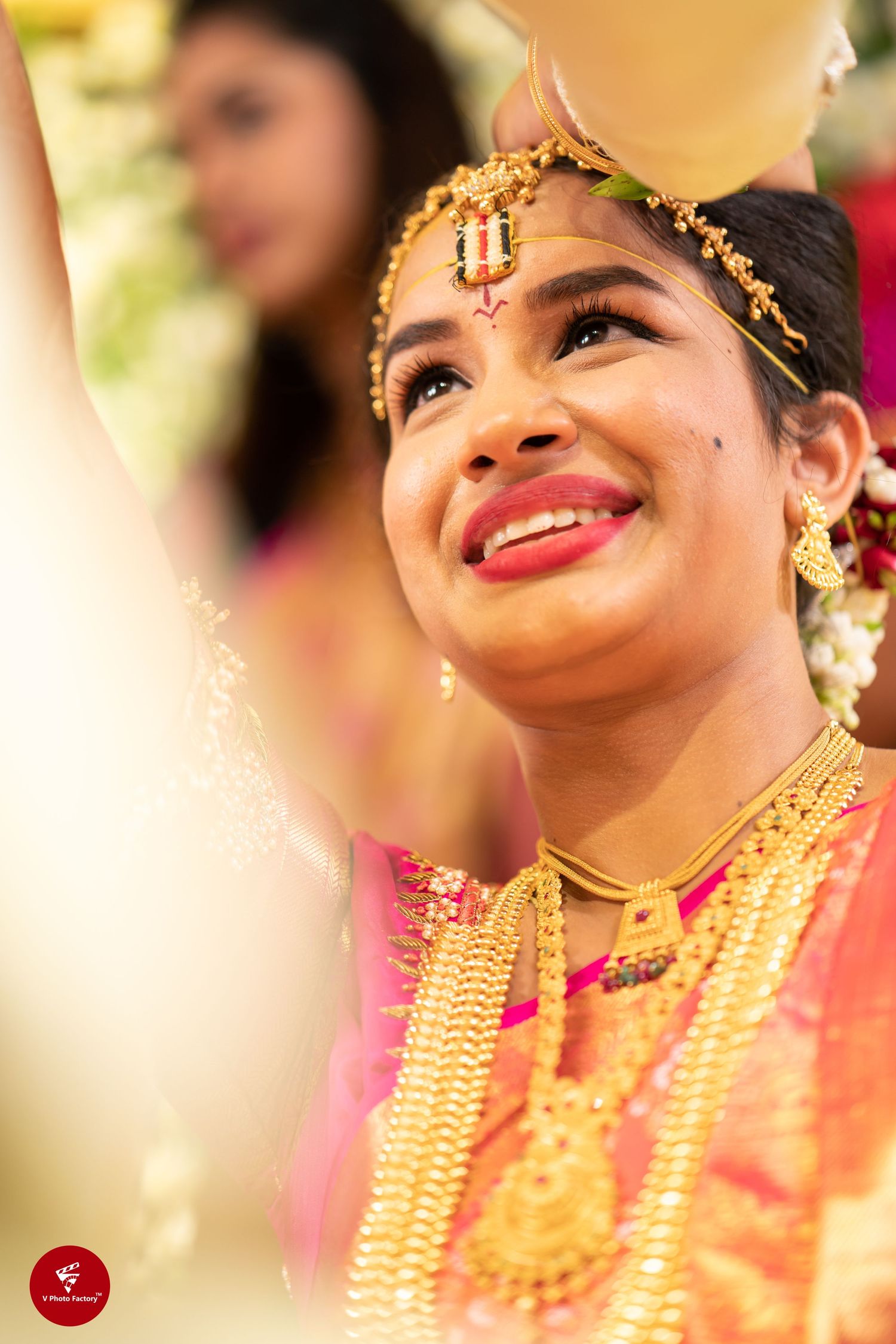 Traditional Indian bride wearing golden jewelry and forehead ornament smiles during wedding ceremony.