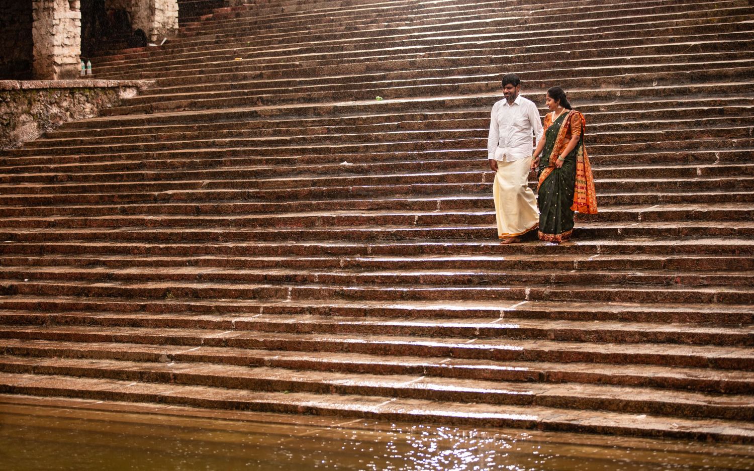 Two people sit together on ancient stone steps by the river in Varanasi, India.