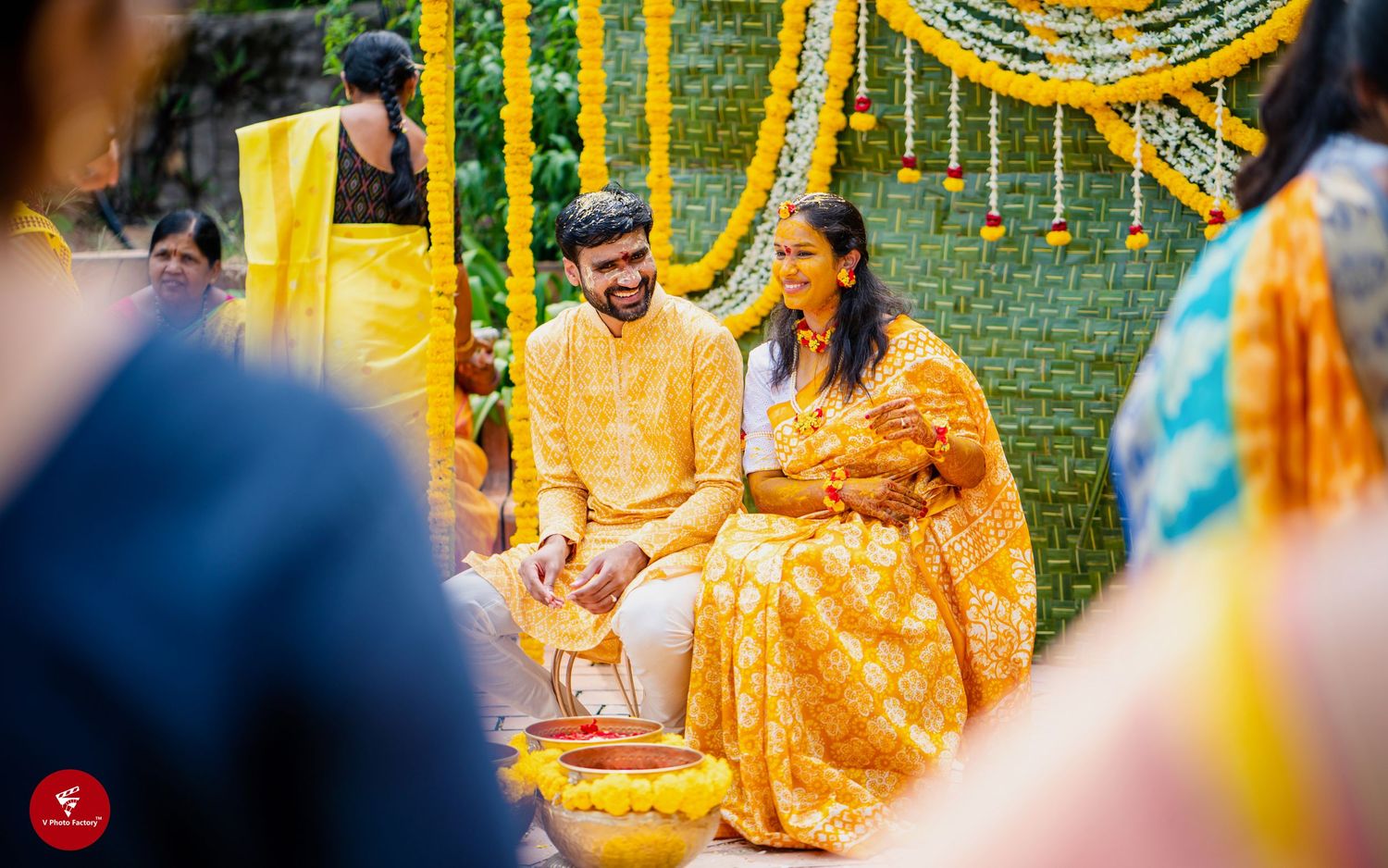 Traditional Indian wedding ceremony with couple in yellow outfits seated under marigold flower decorations.