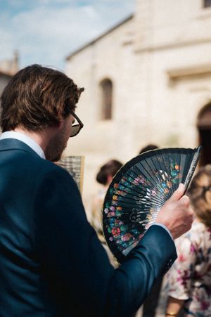 A decorative hand fan being used during an outdoor wedding ceremony.
