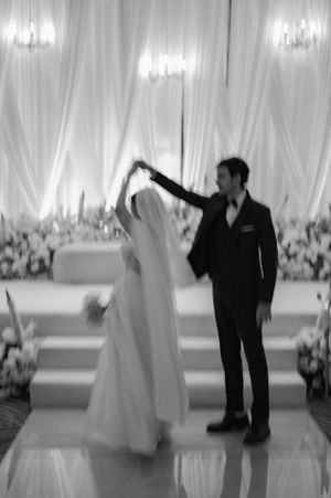 A wedding couple dances together in an elegant white-draped reception venue.