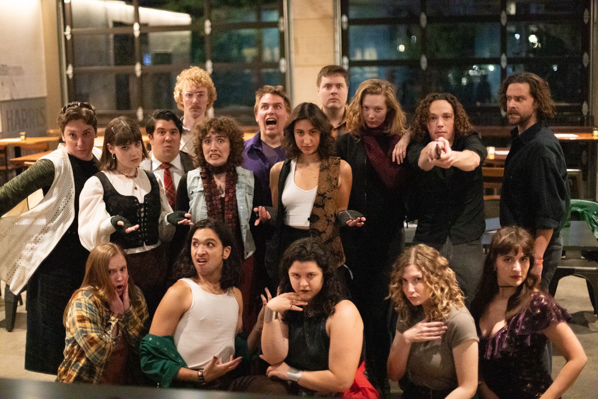 A group of performers in formal attire pose together for a theatrical cast photo in an indoor venue.
