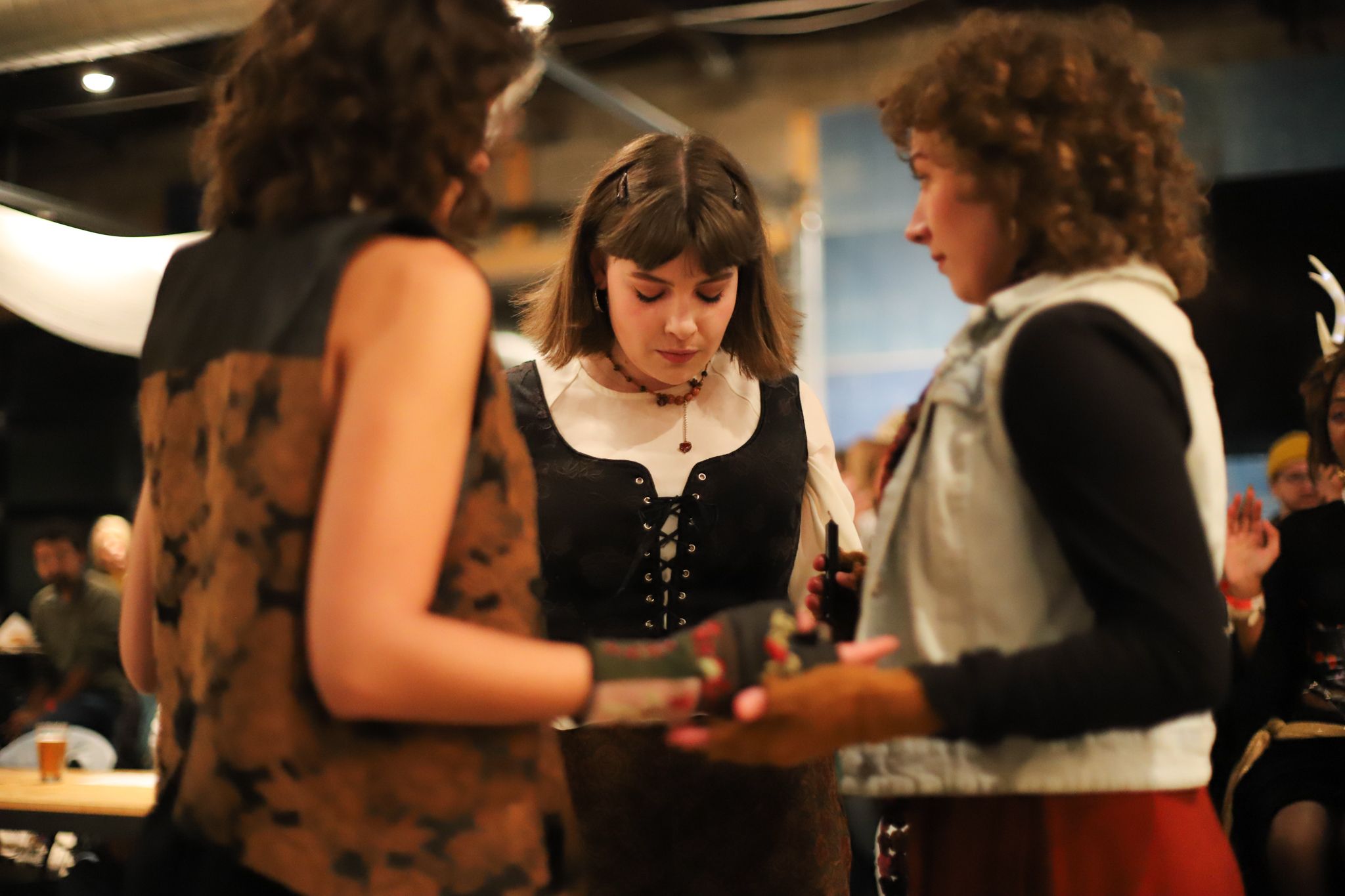 Three performers in period costumes interact backstage during a theatrical production.
