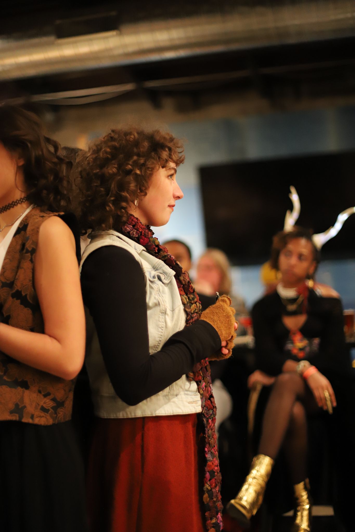 Side view of people at a gathering with curly hair and long scarf, wearing black and white outfit with red accents.