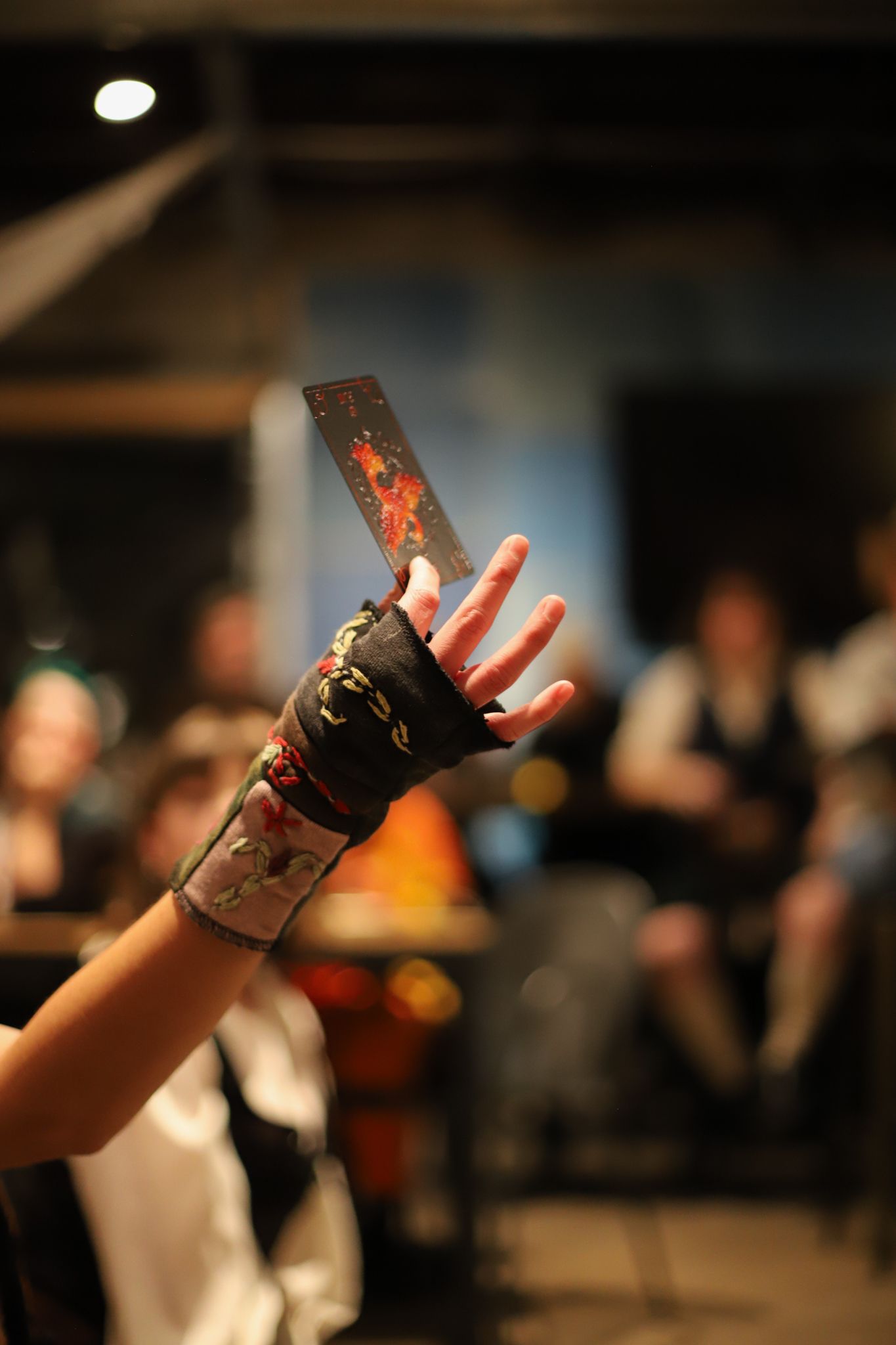 A raised hand wearing a decorative black and red fingerless glove in a dimly lit performance setting.