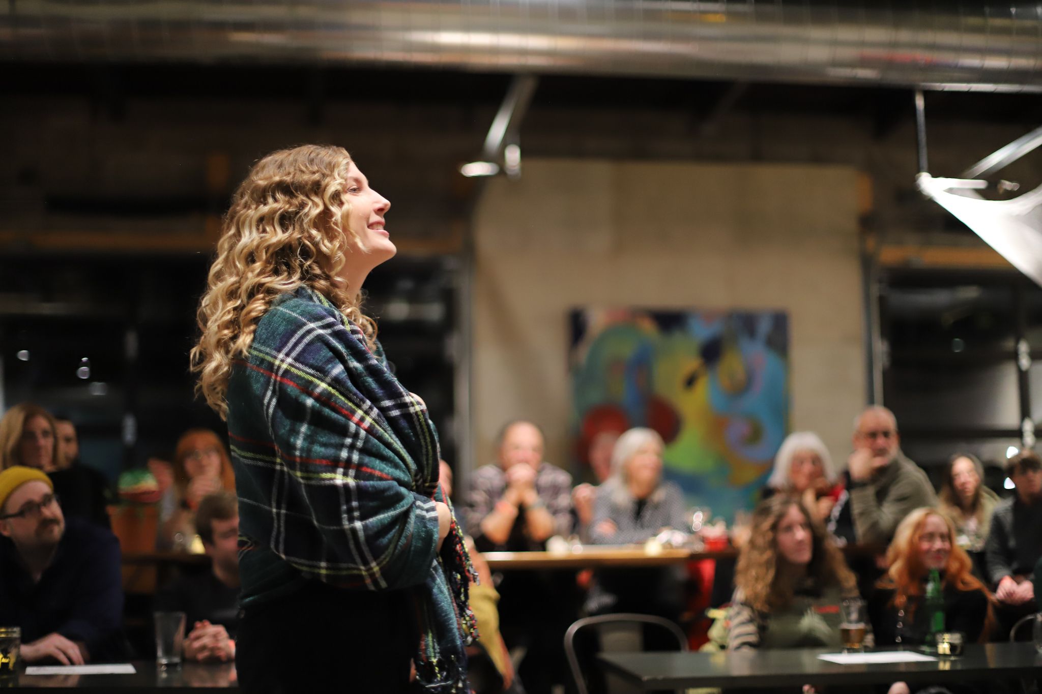 A performer sings passionately in a dark venue while an audience watches from their tables in the background.
