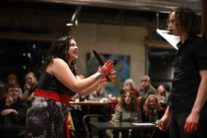 Two performers interact energetically during a theatrical performance in front of a seated audience.