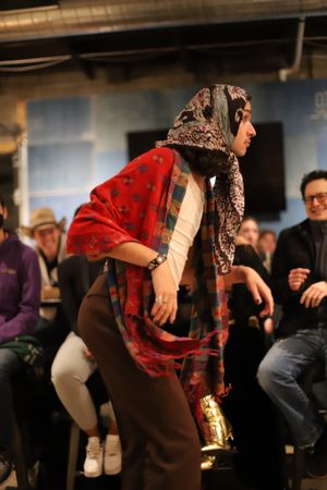 Performer in a red shawl and patterned headscarf dances energetically during a theatrical show.