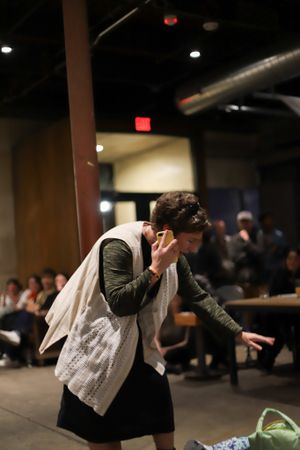 A person in dark clothing and light sweater performs dramatically in a dimly lit indoor space.