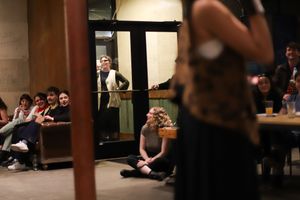 Audience members watch intently in a dimly lit theater space during a performance.