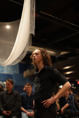 Dramatic performance under hanging white fabric in a dark theater space.