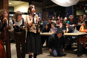 Group performs in casual attire on stage with audience seated at tables in background.