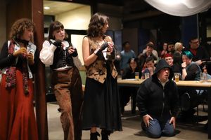A group performs in vintage-inspired costumes before an audience in an indoor gathering space.