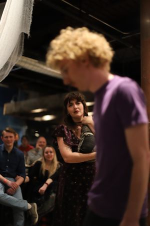 Theater performers interact during a dramatic scene with audience visible in background.
