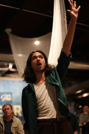 A performer in a green jacket raises their arm dramatically during an expressive theatrical moment.